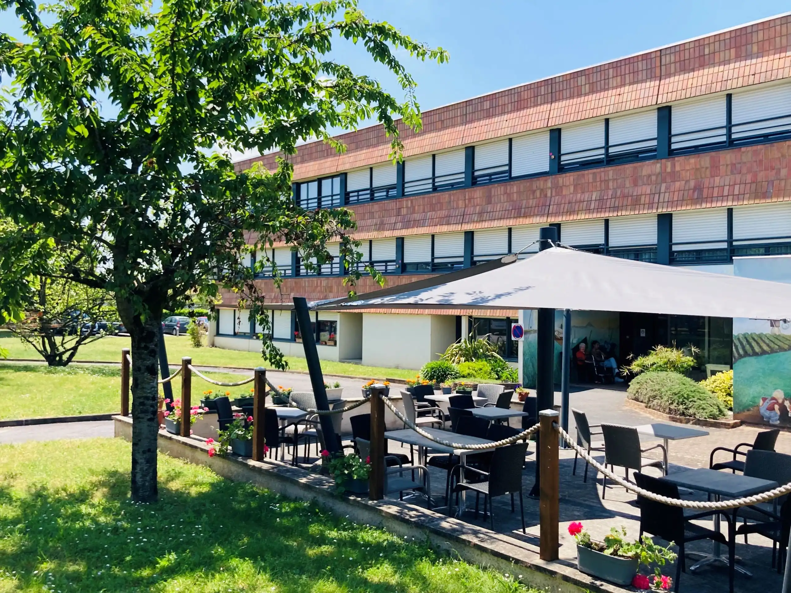 Terrasse extérieure ombragée avec mobilier de jardin et vue sur le bâtiment moderne de l'EHPAD Le Clos du Moulin Divatte-sur-Loire