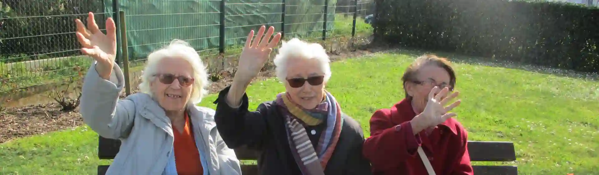 Résidentes souriantes saluant de la main dans le jardin ensoleillé de l'EHPAD Le Clos du Moulin Divatte-sur-Loire