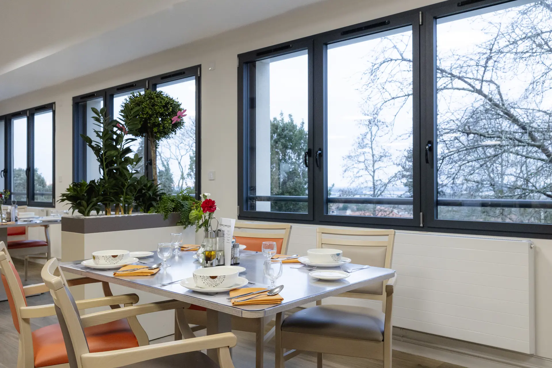 Salle à manger panoramique avec vue sur parc arboré et table dressée dans l'EHPAD Le Clos du Moulin Divatte-sur-Loire